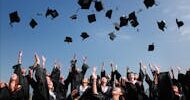 Group of graduates celebrating by throwing caps in the air during a sunny day.